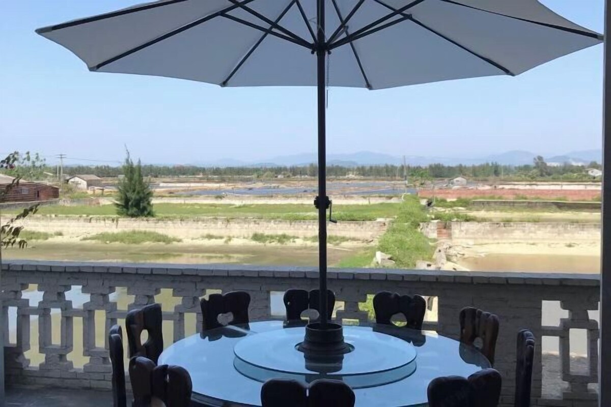 A round table with chairs and an umbrella on a balcony with a view of a river and distant mountains.