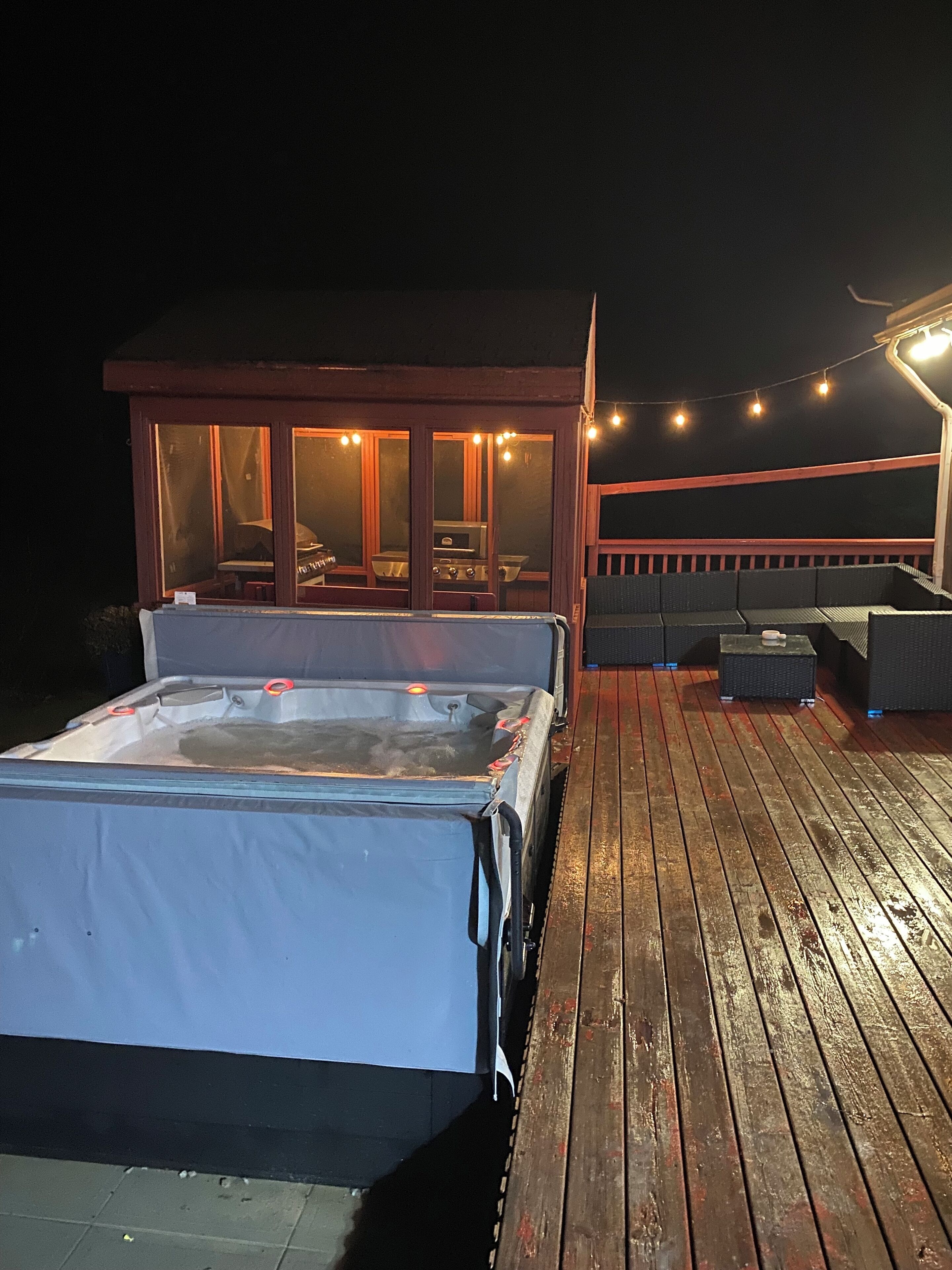 A hot tub on a wooden deck with a glass-enclosed room in the background.