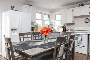 Une cuisine moderne avec des meubles blancs, un réfrigérateur, une cuisinière et une table à manger avec des chaises.