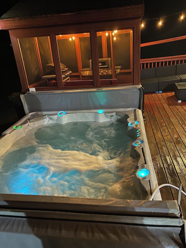 A hot tub with multiple jets, surrounded by a wooden deck and a covered seating area with tables and chairs.