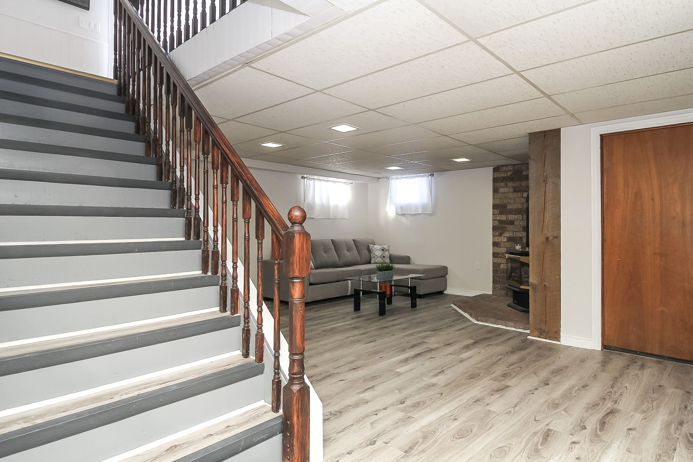 A staircase with wooden balusters leading to a living area with a gray sofa, a coffee table, and a fireplace.