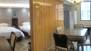 Een hotelkamer met twee bedden, een eettafel, stoelen, een houten scheidingswand en een raam met gordijnen.