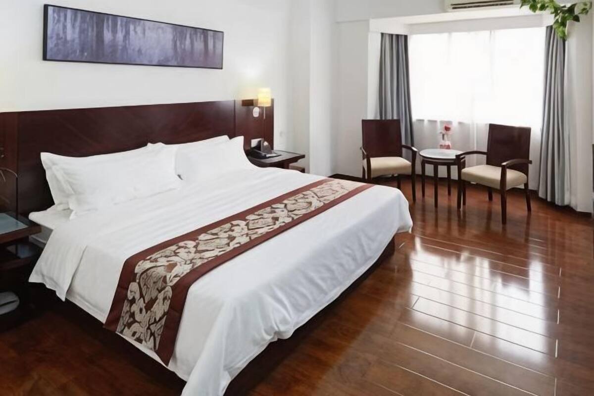 Quarto de hotel com uma cama grande, mesa de cabeceira, escrivaninha e uma cadeira, e vista para o exterior.
