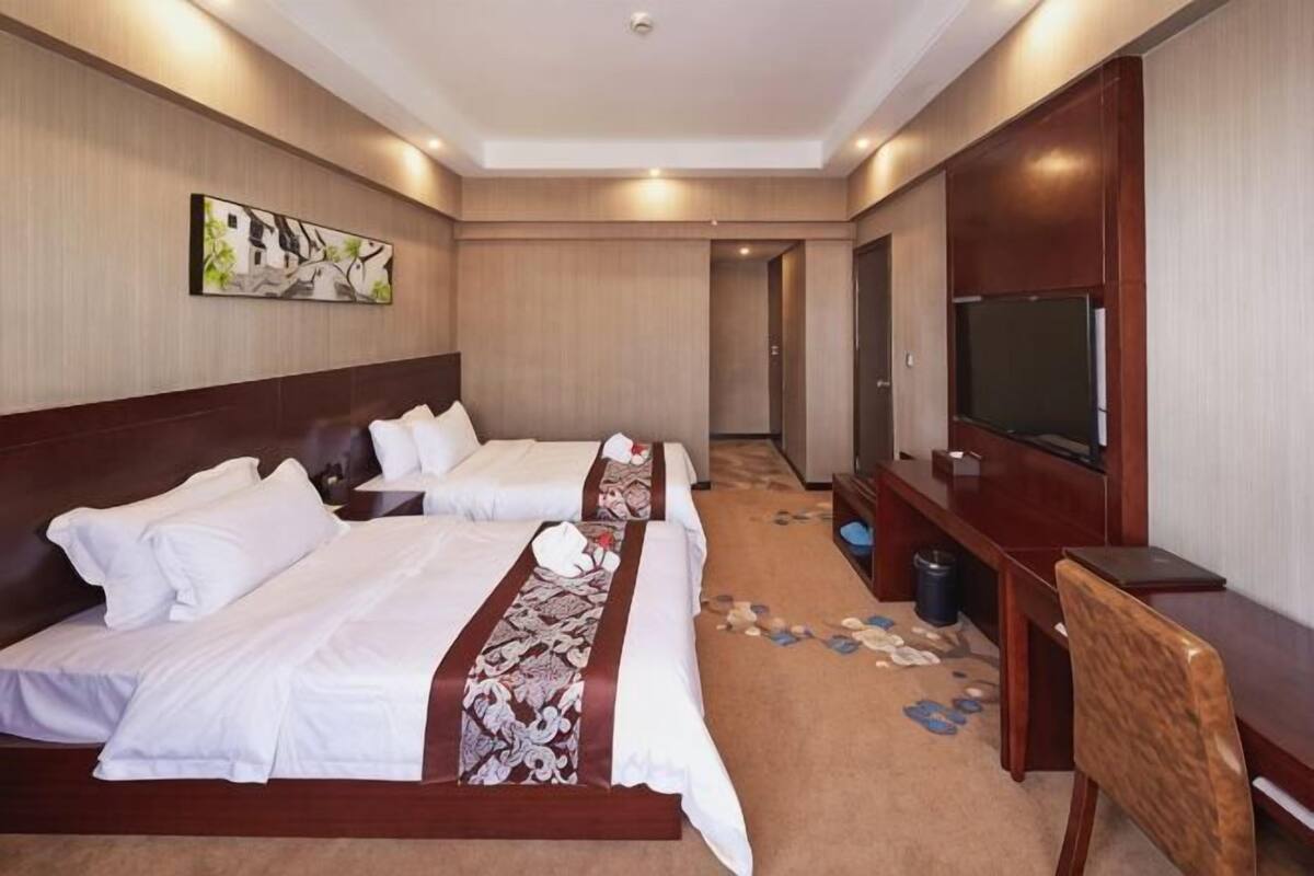 Quarto de hotel com duas camas, televisão, secretária e chão coberto de carpete.