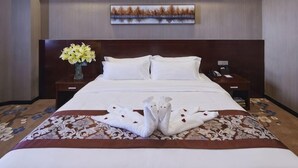 Een hotelkamer met een groot bed, een houten hoofdeinde, een nachtkastje met telefoon, een vaas met bloemen en een schilderij aan de muur.