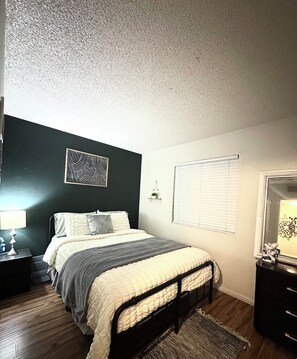 A bedroom with a bed, bedside table, lamp, and a window with blinds. - Comfort Apartment (Las Vegas)