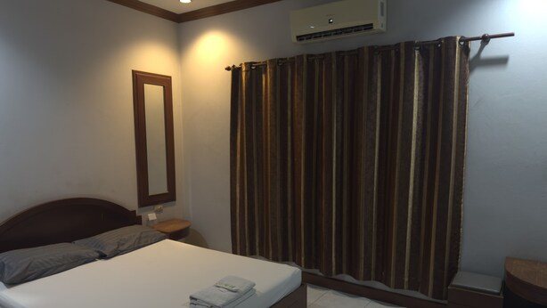 A hotel room with a single bed, a nightstand, a mirror, an air conditioning unit, and a curtain. - Maingam Resort (Si Prachan)