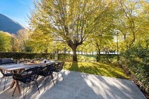 Area pranzo all'aperto con tavolo e sedie, circondata da alberi e vista su un corpo d'acqua.