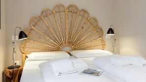 Ein Bett mit einem gewobenen Kopfteil, weißer Bettwäsche, zwei Nachttischlampen und einer Zeitschrift auf dem Bett.