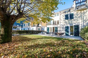 A courtyard with a tree, grass, and scattered leaves.