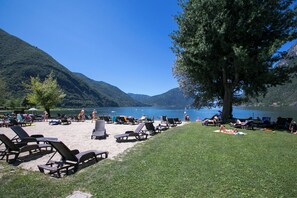 A lakeside beach with lounge chairs and a grassy area.