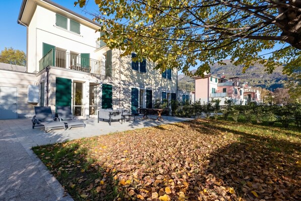A modern building with a balcony, outdoor seating, and a garden with fallen leaves.