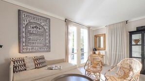 Ein Zimmer mit einer Couch, zwei Korbstühlen, einem runden Tisch, einem großen gerahmten Kunstwerk und einem Schrank mit Spiegel.