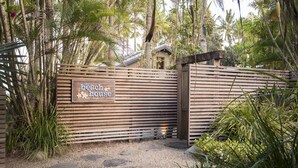 Une porte en bois, sur laquelle on peut lire l’inscription « la maison de plage », est entourée d’une végétation tropicale.