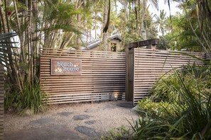 Una puerta de madera con un letrero que dice "the beach house", rodeada de follaje tropical.