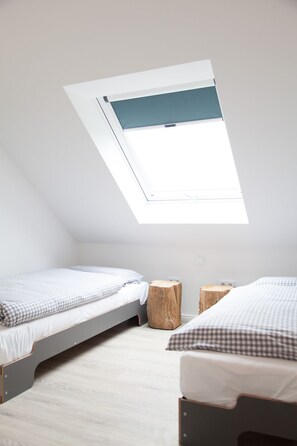 Un dormitorio pequeño y moderno con dos camas individuales, un tragaluz y suelo de madera clara.