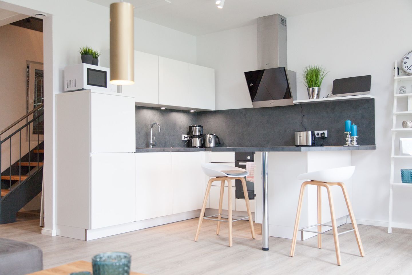 A modern kitchen with white cabinets, a black countertop, and two wooden stools.