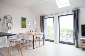 Eine moderne Küche mit Essbereich, großen Schiebeglasfenstern zum Balkon und einem an der Wand montierten Fernseher.