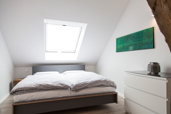 Ein Schlafzimmer mit Bett, Fenster, einem grünen Kunstwerk und einer Kommode.
