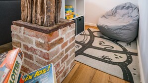 Una sala acogedora con una chimenea de ladrillo, un sillón de peluche gris y una alfombra con motivos de carretera.