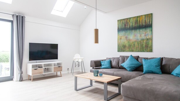 Una sala de estar moderna con un televisor de pantalla plana, un sofá con cojines color turquesa, una mesa de centro de madera y un cuadro en la pared.