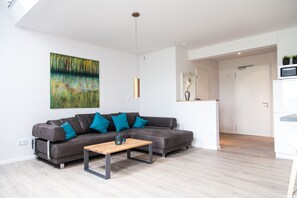 Una sala de estar moderna con un sofá gris, cojines turquesa, una mesa de centro de madera y un cuadro abstracto grande en la pared.