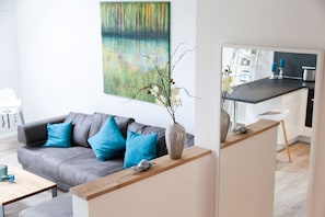 Ein modernes Wohnzimmer mit einem grauen Sofa, blauen Kissen, einem Holztisch und einer dekorativen Vase mit Zweigen und Blumen.