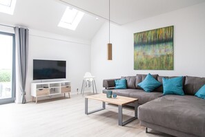 Un salon moderne avec un téléviseur à écran plat, un canapé agrémenté de coussins turquoise, une table basse en bois et un tableau accroché au mur.