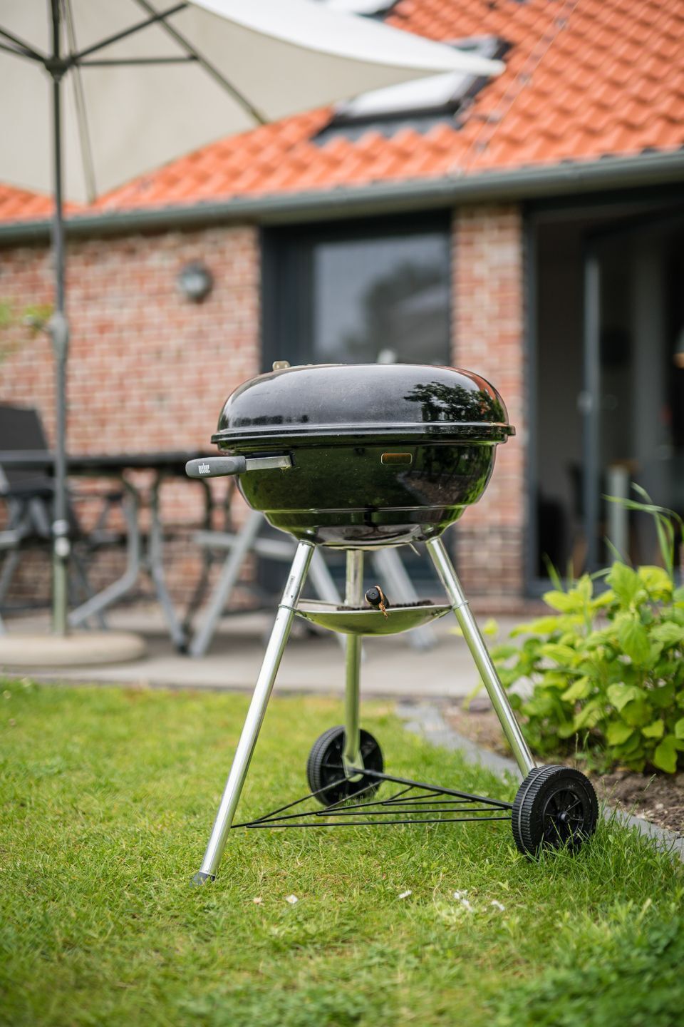 A portable barbecue grill with wheels, set on a grassy lawn.