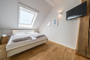 Ein modernes Schlafzimmer mit Dachfenster, einem Bett mit karierter Bettwäsche, einem Wand-Fernseher und Holzboden.