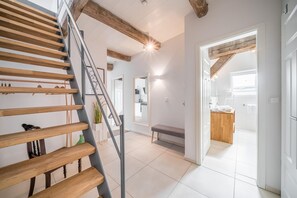 A modern interior with a wooden staircase, a bench, and a kitchen area visible through an open doorway.