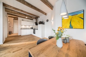 Eine moderne Küche mit weißen Schränken, einem Holztisch und einem großen, gelben Gemälde an der Wand.