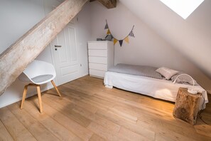 A bedroom with a sloped ceiling, a white chair, a bed with checkered bedding, a dresser, and a wooden post with a power outlet.