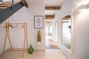 A modern interior with a wooden staircase, a coat rack, a framed inspirational quote, a potted plant, and a view into a dining area.