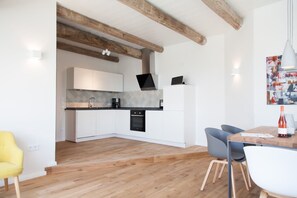 A modern kitchen with white cabinets, a black oven, and a wooden ceiling. There is a dining area with a table and chairs.