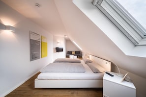 Une chambre moderne avec un plafond de style industriel, un lit avec une literie à carreaux, une table de chevet avec une lampe et un téléviseur fixé au mur.