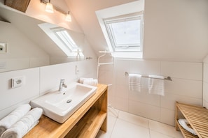 Une salle de bain moderne dotée d’un puits de lumière, d’un grand miroir, d’un meuble-lavabo en bois et d’un porte-serviettes.