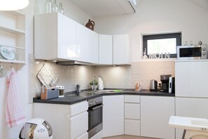 A modern kitchen with white cabinets, a black countertop, a stove, a sink, and a microwave.