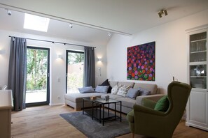 A modern living room with a sofa, armchair, and coffee table, a large window with curtains, and a colorful abstract painting on the wall.