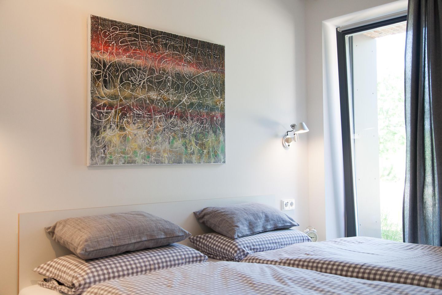 Quarto com duas camas, um quadro abstrato grande na parede, luminária de cabeceira e janela com cortinas.