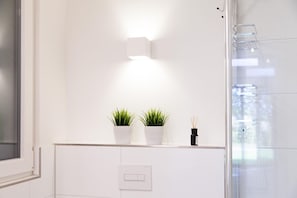 A modern bathroom with a white countertop, two potted plants, a diffuser, and a glass shower enclosure.