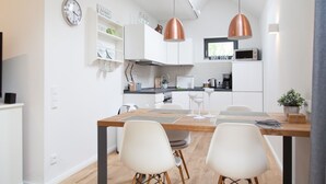 Une cuisine moderne avec des meubles blancs, une table à manger en bois et deux lampes suspendues.