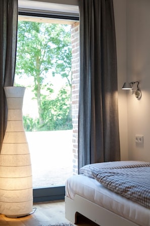 Ein Schlafzimmer mit einem Bett, einer Stehlampe, einem Fenster mit Vorhängen und einer Wandleuchte.