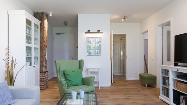 Un salon avec un fauteuil vert, une table basse en verre, un meuble blanc et un téléviseur posé sur un meuble blanc.