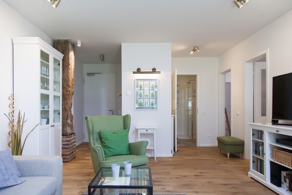 Ein Wohnzimmer mit einem grünen Sessel, einem Glastisch, einer weißen Kommode und einem Fernsehgerät auf einem weißen Schrank.