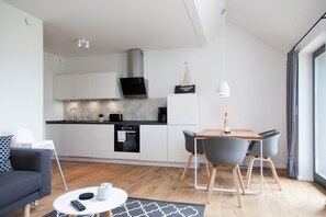 A modern kitchen with white cabinets, a black oven, and a dining area with a wooden table and grey chairs.