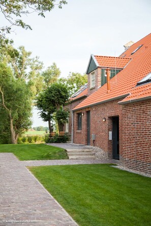 A brick building with a red-tiled roof, a paved pathway, and a well-maintained lawn.