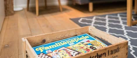 Una caja de madera con libros etiquetados como “Wein aus deutschen Land” en una sala de estar con un sillón amarillo, sofá gris y alfombra blanco y negro.