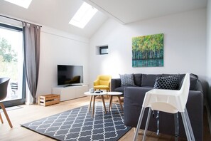 Moderni olohuone, jossa on litteänäyttöinen televisio, keltainen nojatuoli, harmaa sohva ja taulu seinällä.