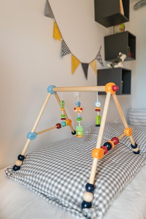 Um móbile infantil com contas coloridas e figuras de animais, colocado sobre um travesseiro xadrez em uma cama.